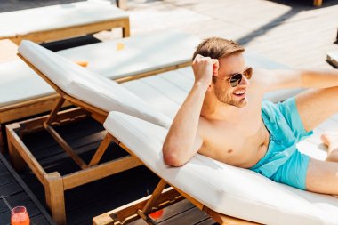 happy shirtless man in sunglasses lying on lounger at resort