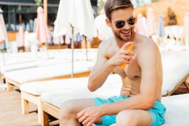 shirtless man sitting on lounger and applying sunscreen at resort