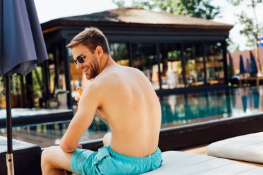 shirtless man sitting on lounger and applying sunscreen at resort