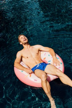 yüzme havuzunda yüzme halkası üzerinde yatan gülen gömleksiz adam