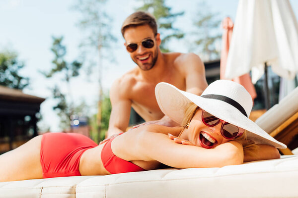 smiling man in sunglasses doing massage for girlfriend at resort