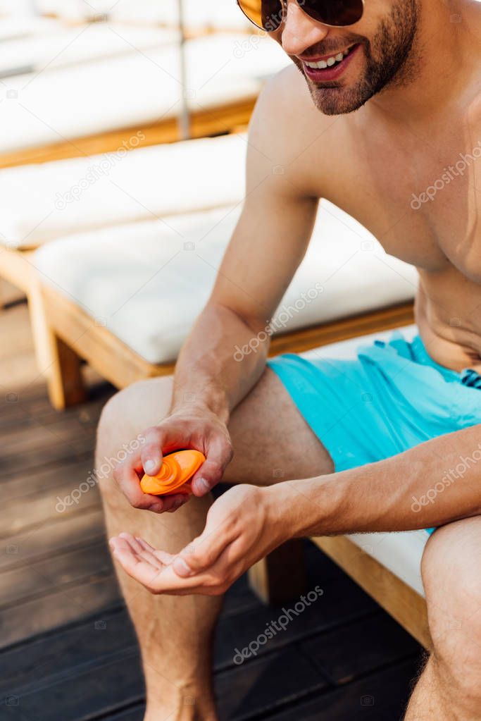 partial view of shirtless man sitting on lounger and applying sunscreen at resort