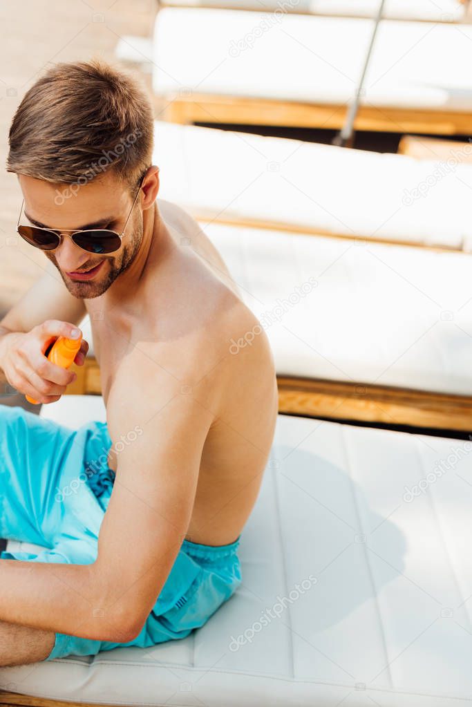 shirtless man sitting on lounger and applying sunscreen at resort