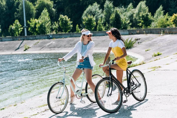 Szczęśliwy Blond Brunette Dziewczyny Rowerami Patrząc Siebie Pobliżu Rzeki Lecie — Zdjęcie stockowe