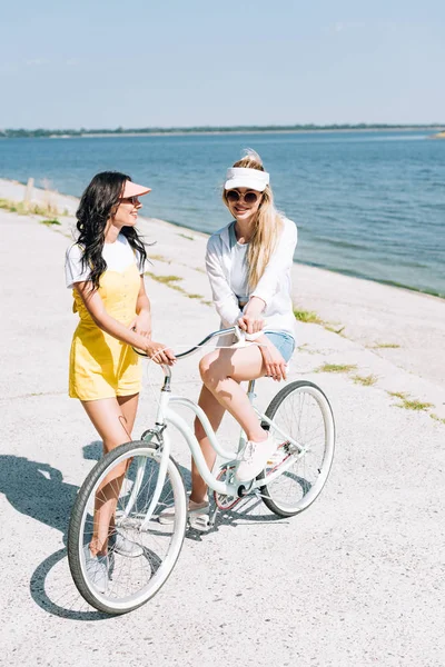 Sonrientes Chicas Rubias Morenas Con Bicicleta Cerca Del Río Verano —  Fotos de Stock