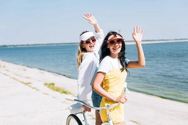 Meninas Loiras Morenas Com Bicicleta Acenando Mãos Perto Rio Verão — Fotografia de Stock
