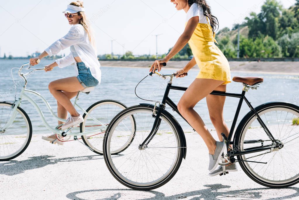 side view of blonde and brunette girls riding bikes near river in summer