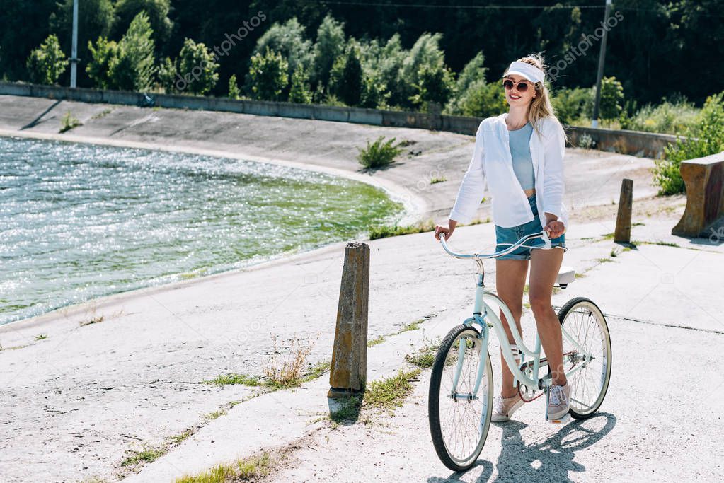 blonde beautiful girl riding bicycle near river in summer