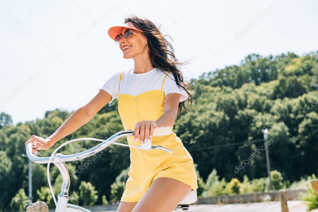 low angle view of smiling brunette beautiful girl riding bicycle in summer