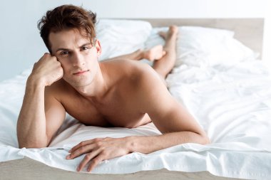 yatakta yatarken kameraya bakan gömleksiz adamın seçici odak 