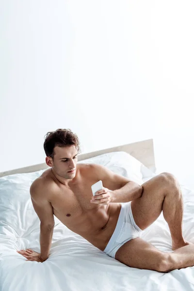 Yatakta Otururken Akıllı Telefon Kullanarak Seksi Gömleksiz Adam — Stok fotoğraf