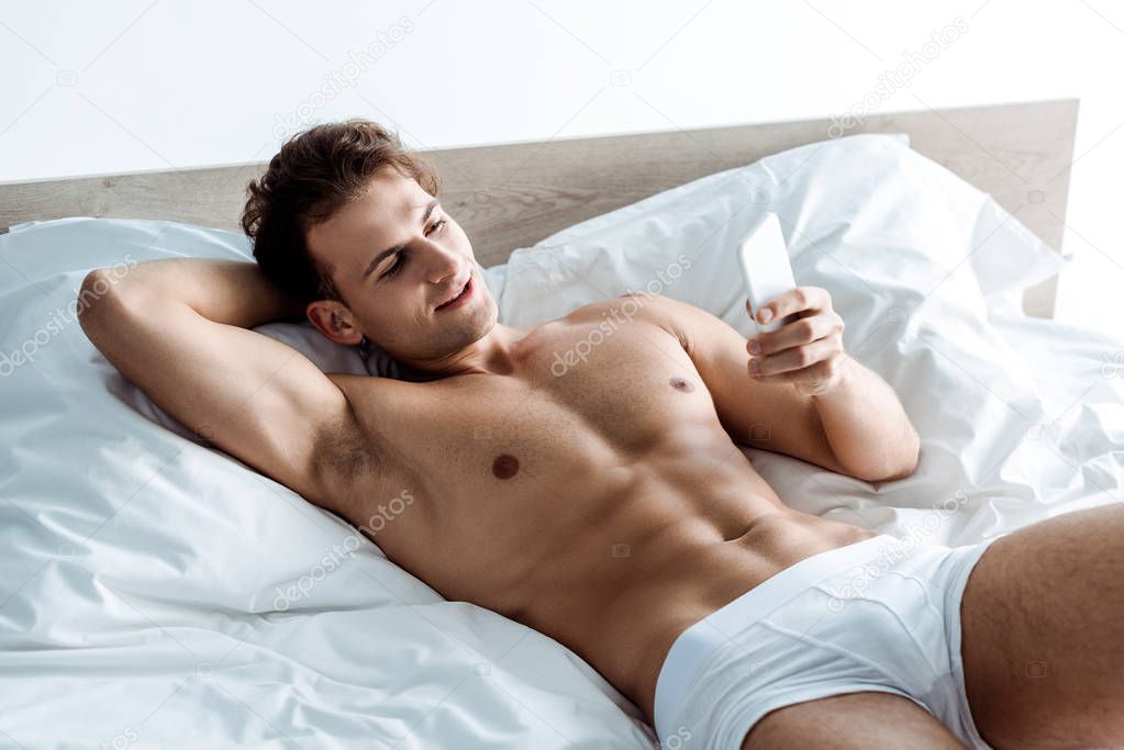handsome shirtless man using smartphone while lying on bed