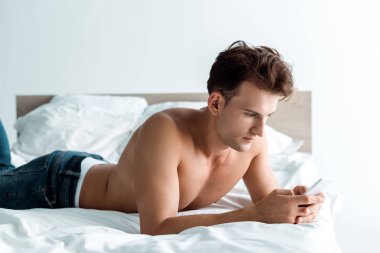 yatak odasında akıllı telefon kullanarak kot pantolon yakışıklı ve gömleksiz adam 