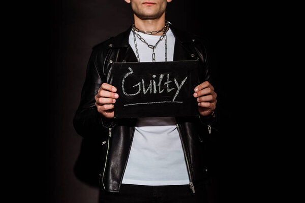 cropped view of man holding chalk board with guilty lettering on black  