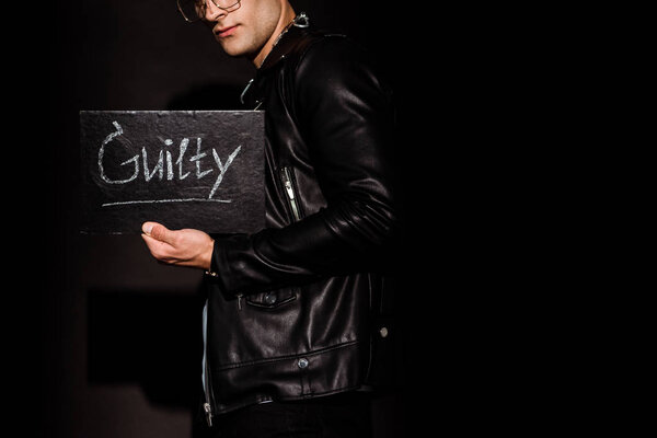 cropped view of young man holding chalk board with guilty lettering on black  