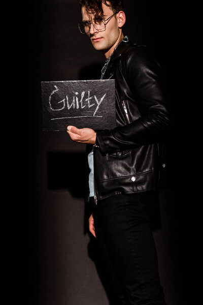 stylish man holding chalk board with guilty lettering on black  