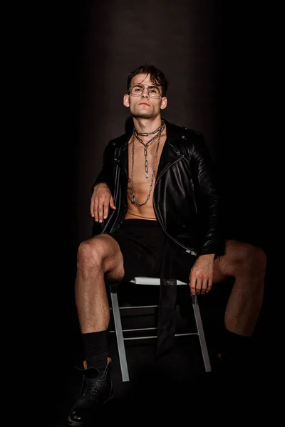 brutal young man in leather jacket sitting on black