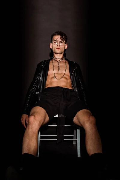 brutal young man in glasses and leather jacket sitting on black