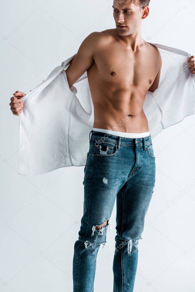 handsome man standing in denim jeans and undressing isolated on white 
