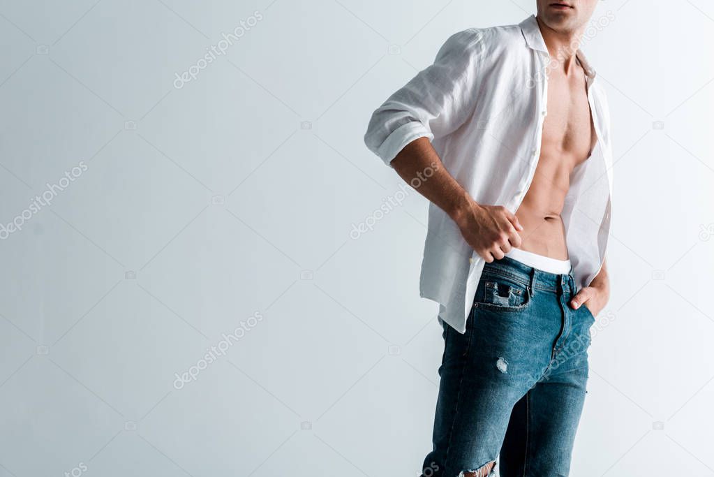 cropped view of sexy man in jeans and shirt standing with hand in pocket on white 