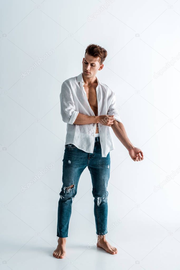 handsome man touching shirt while standing on white 