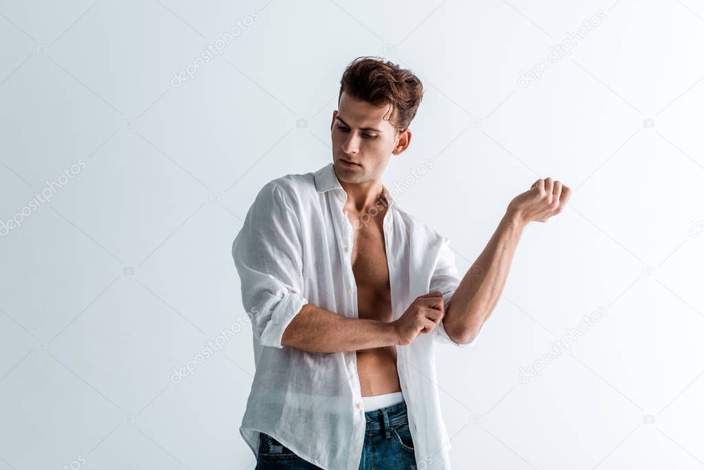 handsome young man touching shirt while standing on white 