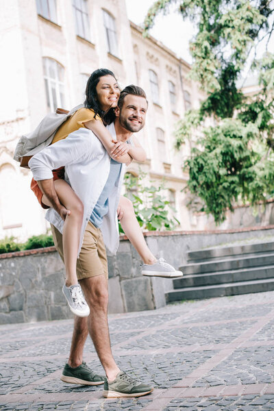 happy bearded man piggybacking cheerful girl near building 