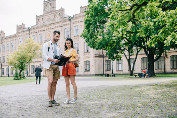KYIV, UKRAINE - MAY 28, 2019: handsome man and attractive girl standing near building with map 