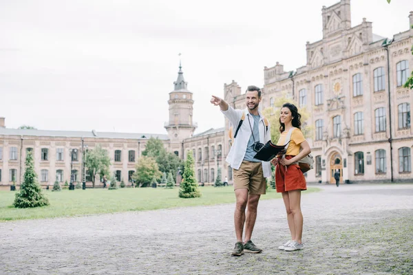 Przystojny Mężczyzna Wskazując Palcem Trzymając Mapę Pobliżu Atrakcyjne Dziewczyny Kampusu — Zdjęcie stockowe