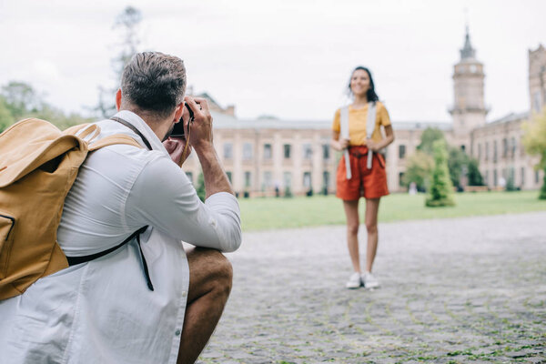 selective focus of man taking photo of happy woman standing near building 