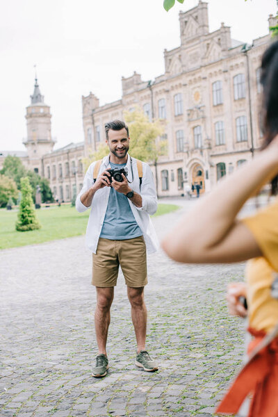 selective focus of happy man holding digital camera near girl and university campus 