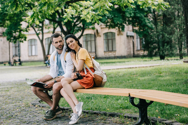 cheerful man and woman sitting on bench with map 