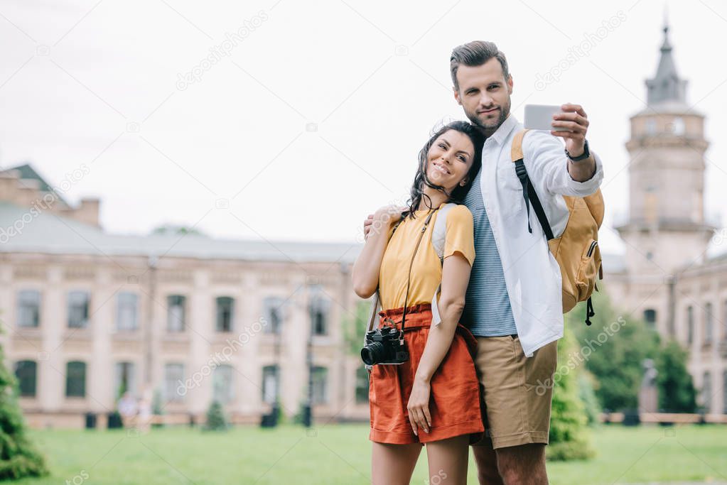 happy bearded man and attractive woman taking selfie near building 