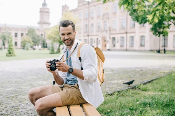 Счастливый Мужчина Смотрит Камеру Держит Цифровой Фотоаппарат Сидя Скамейке — стоковое фото