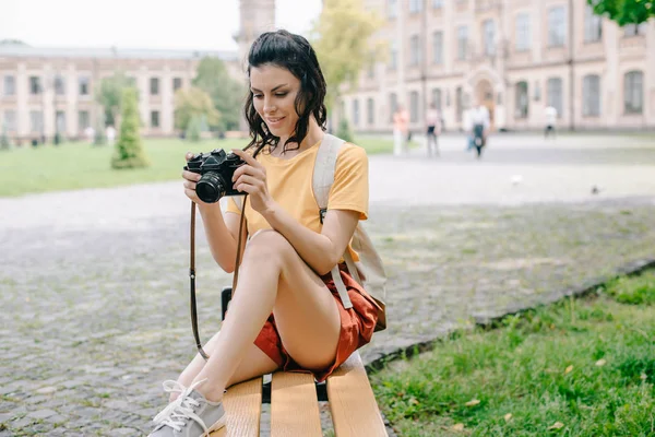 Atrakcyjna Młoda Kobieta Patrząc Aparat Cyfrowy Siedząc Ławce Pobliżu Uniwersytetu — Zdjęcie stockowe