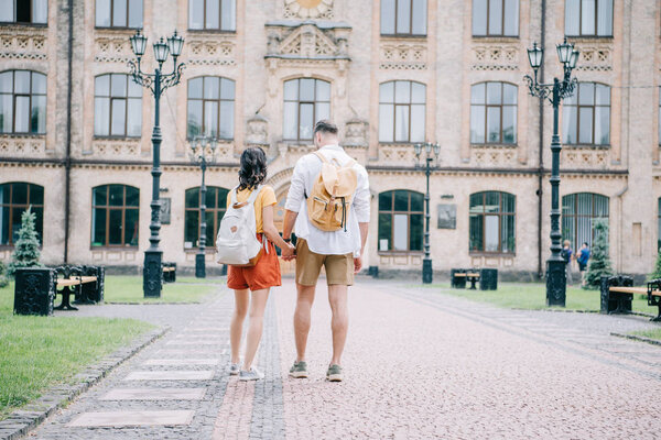 вид сзади купе, держащегося за руки, стоя возле здания
 