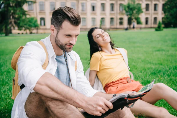 选择焦点的快乐男人拿着地图靠近女人坐在草地上 — 图库照片