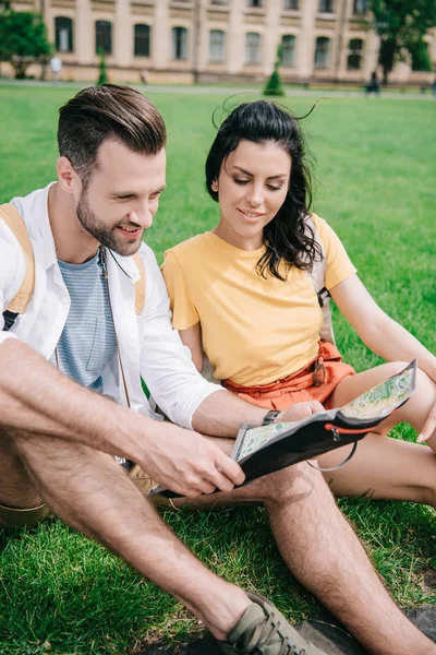 幸せな男女が草の上に座って地図を見ている — ストック写真