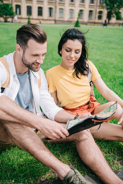 happy man and woman sitting on grass and looking at map 