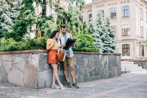 bearded man and attractive woman standing near building with atlas 