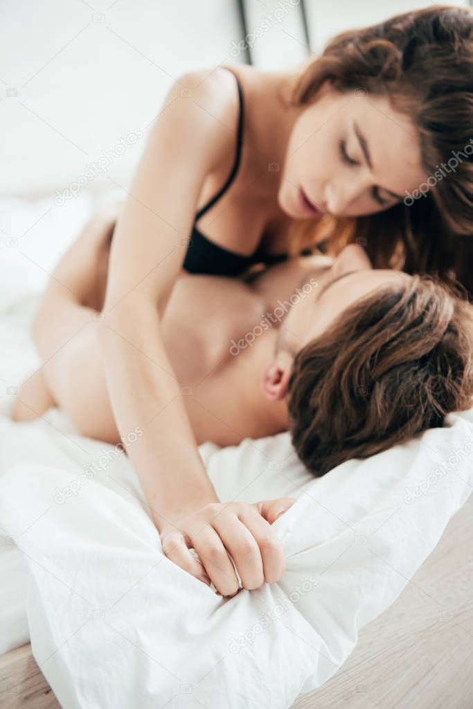 selective focus of attractive girlfriend in black underwear hugging and kissing boyfriend in bed