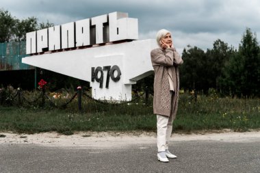 Pripyat, Ukrayna - 15 Ağustos 2019: pripyat harfleri ve kulakları kapsayan anıtın yanında duran emekli kadın 