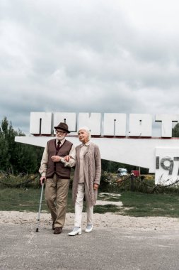 Pripyat, Ukrayna - 15 Ağustos 2019: Pripyat harfleri ile anıtın yakınında yürüyen emekli çift