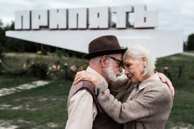 Pripyat, Ukrayna - 15 Ağustos 2019: pripyat harfleri ile anıtın yakınında sarılma kıdemli çift seçici odak 