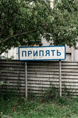 PRIPYAT, UKRAINE - AUGUST 15, 2019: sign with pripyat lettering near fence and trees  clipart