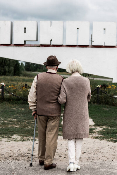 PRIPYAT, UKRAINE - AUGUST 15, 2019: back view of retired husband and wife standing near monument with letters