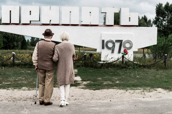 PRIPYAT, UKRAINE - AUGUST 15, 2019: back view of retired couple standing near monument with pripyat letters