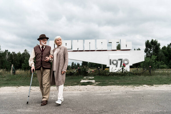 PRIPYAT, UKRAINE - AUGUST 15, 2019: senior couple walking near monument with pripyat letters