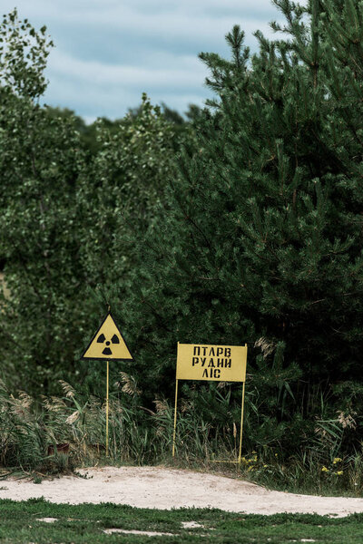 PRIPYAT, UKRAINE - AUGUST 15, 2019: chernobyl zone with yellow warning signs near green trees 