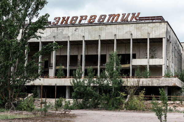 ПРИПЯТ, УКРАИНА - 15 августа 2019 года: здание с энергичными надписями возле зеленых деревьев в Чернобыле
 